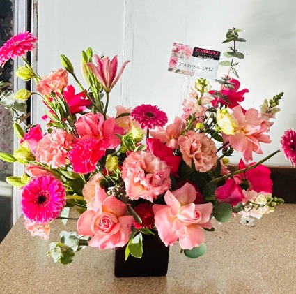 Arrangement in a square vase made of roses, carnations, gerber daysies, lilys, etc.