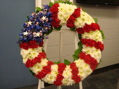 Red, White and Blue wreath with white. (S)  and red Carnations, delphium and white cushion poms with ribbons and stars.